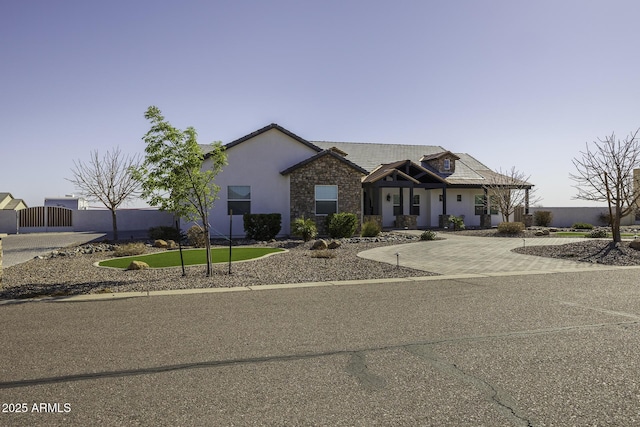 view of front of house with fence, stucco siding, stone siding, driveway, and a gate