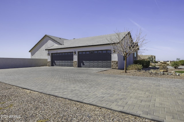 view of side of property featuring decorative driveway, stone siding, a garage, and stucco siding