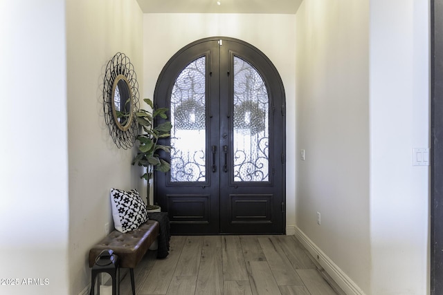 foyer entrance with arched walkways, light wood-style flooring, french doors, and baseboards