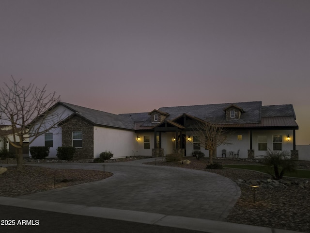 view of front of property featuring decorative driveway, stone siding, and stucco siding