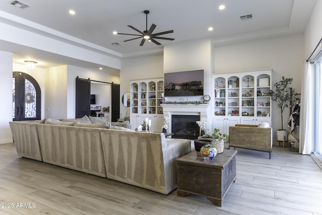 living room with visible vents, a barn door, recessed lighting, light wood-style flooring, and a glass covered fireplace