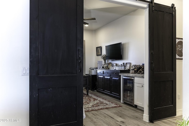 kitchen with a barn door, beverage cooler, light wood-style floors, and ceiling fan