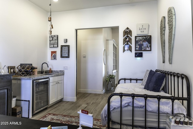 bedroom with a sink, wine cooler, light wood-style floors, wet bar, and baseboards