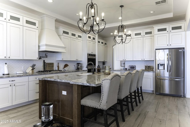 kitchen with visible vents, a tray ceiling, custom range hood, appliances with stainless steel finishes, and a sink