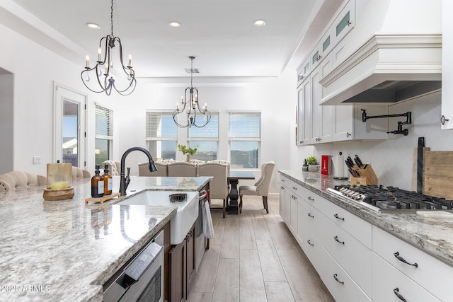 kitchen with a sink, stainless steel gas stovetop, light stone countertops, custom exhaust hood, and a chandelier