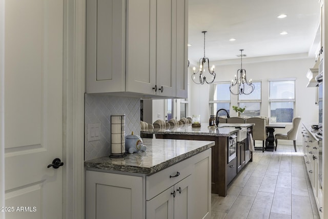 kitchen featuring pendant lighting, light stone counters, a sink, stainless steel oven, and decorative backsplash