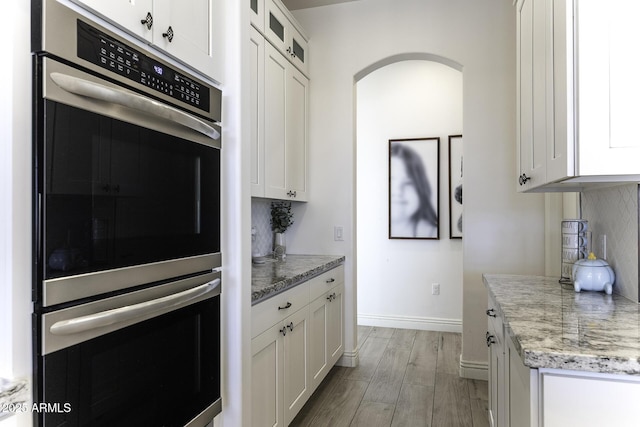 kitchen with stainless steel double oven, white cabinets, glass insert cabinets, and decorative backsplash