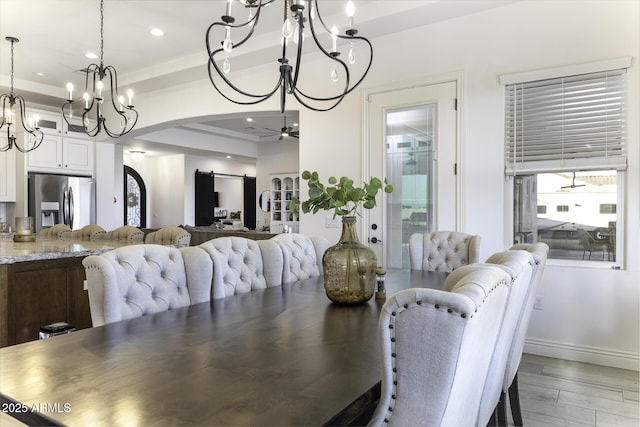 dining space with a barn door, recessed lighting, ceiling fan with notable chandelier, light wood-style floors, and arched walkways