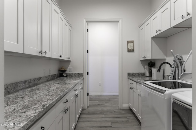 kitchen featuring baseboards, washing machine and clothes dryer, light wood-style flooring, a sink, and white cabinets