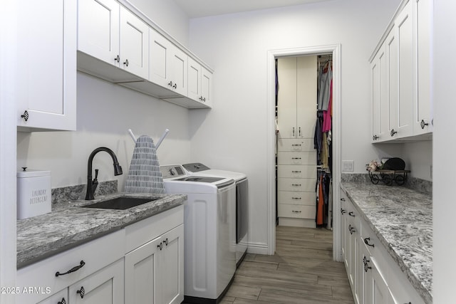 clothes washing area with a sink, light wood-style flooring, cabinet space, and washing machine and clothes dryer