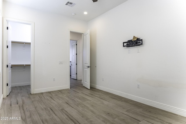 unfurnished bedroom featuring visible vents, baseboards, a walk in closet, and light wood-style floors