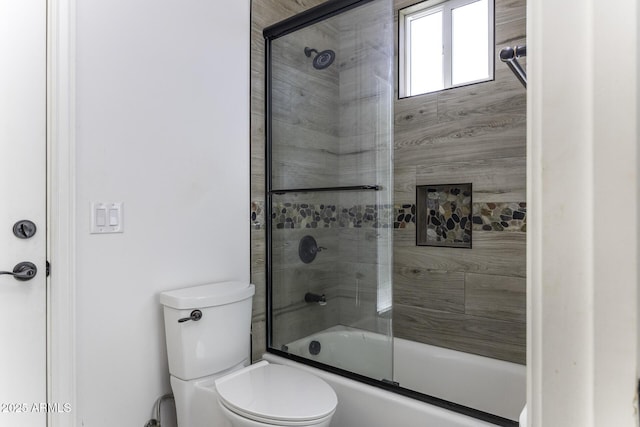 bathroom featuring toilet and bath / shower combo with glass door