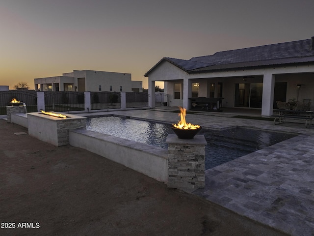 pool at dusk with a patio, fence, a fenced in pool, and an outdoor fire pit