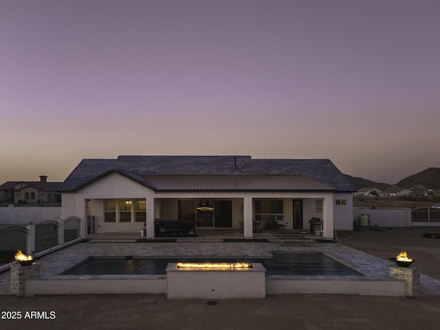 rear view of property featuring a gate, metal roof, fence, and an outdoor fire pit