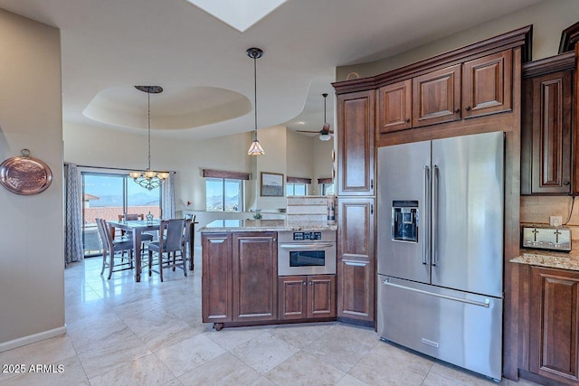 kitchen with hanging light fixtures, backsplash, stainless steel appliances, light stone counters, and a tray ceiling