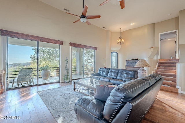 living room with a towering ceiling, wood-type flooring, and ceiling fan with notable chandelier