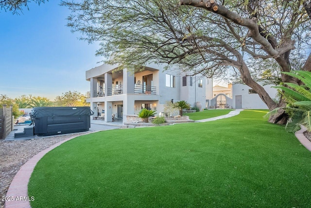 back of house featuring a lawn, a hot tub, and a balcony