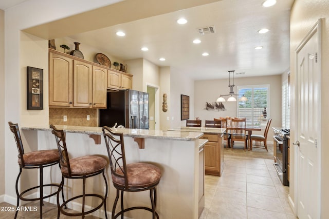 kitchen with visible vents, a peninsula, stainless steel appliances, decorative backsplash, and a kitchen bar