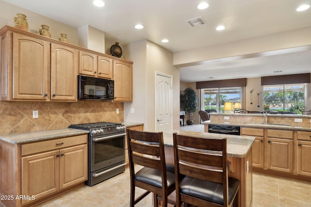 kitchen featuring a breakfast bar area, light stone countertops, a sink, black appliances, and backsplash