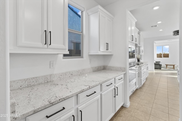 kitchen with oven, light tile patterned floors, white cabinets, and light stone counters