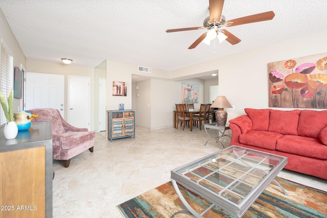 living room with a ceiling fan, visible vents, and a textured ceiling