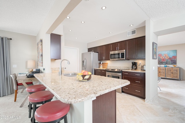 kitchen with a peninsula, appliances with stainless steel finishes, a sink, and a breakfast bar