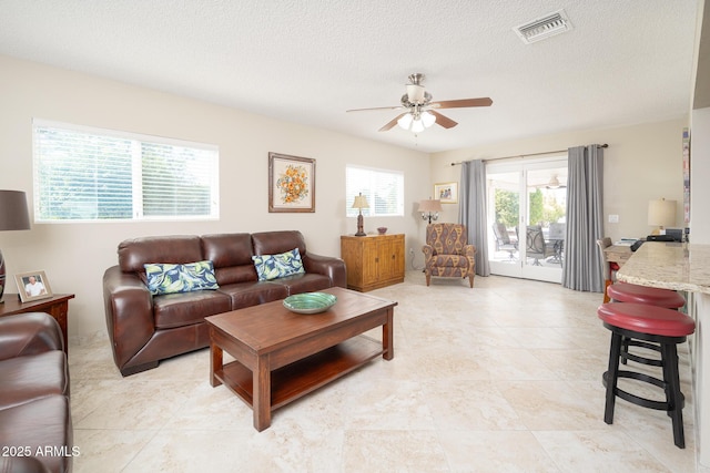 living room with a ceiling fan, visible vents, and a textured ceiling