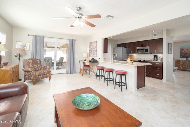 living area with a ceiling fan, visible vents, and a textured ceiling