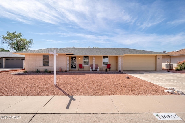 single story home featuring a porch, an attached garage, cooling unit, brick siding, and driveway