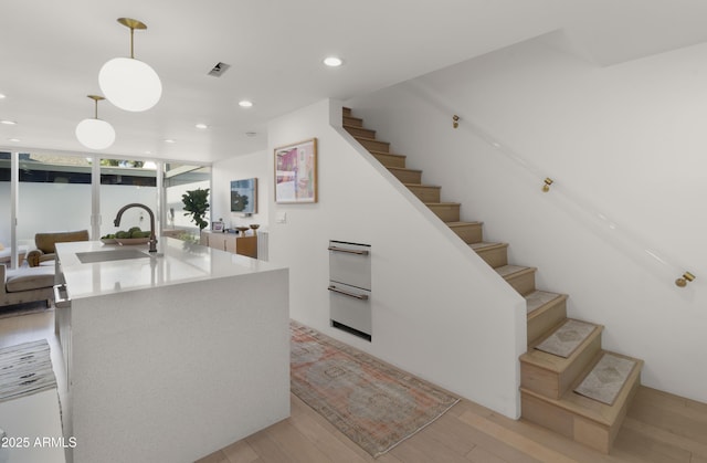 kitchen with a sink, light wood-style flooring, recessed lighting, visible vents, and pendant lighting