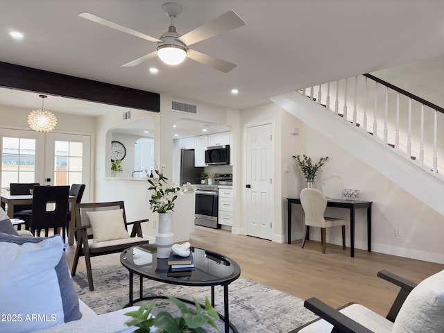 living room featuring light wood-type flooring, ceiling fan with notable chandelier, french doors, and beamed ceiling