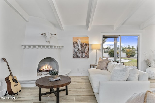 living room with beamed ceiling, baseboards, a warm lit fireplace, and light wood-style flooring