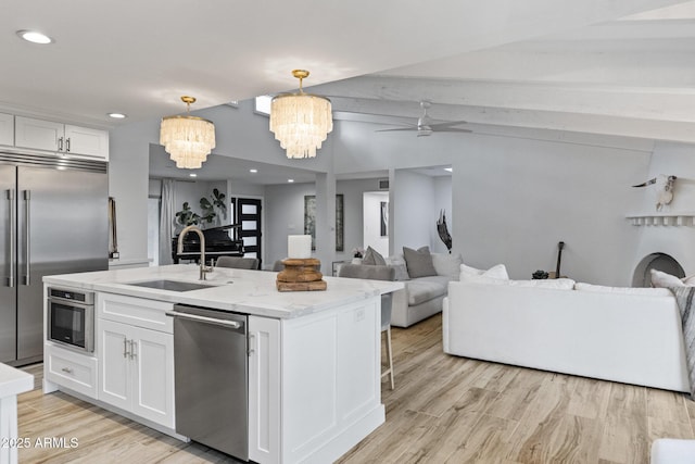 kitchen featuring a center island with sink, lofted ceiling, stainless steel appliances, a ceiling fan, and a sink