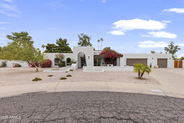 pueblo revival-style home with stucco siding, a garage, and concrete driveway