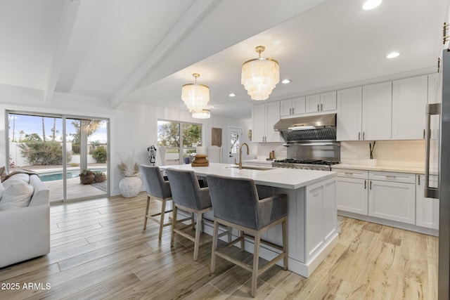 kitchen with under cabinet range hood, a sink, white cabinetry, an inviting chandelier, and decorative backsplash
