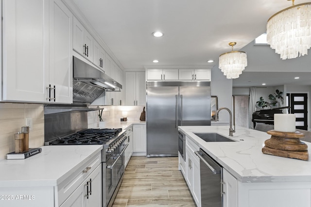 kitchen featuring a sink, white cabinets, under cabinet range hood, a notable chandelier, and premium appliances