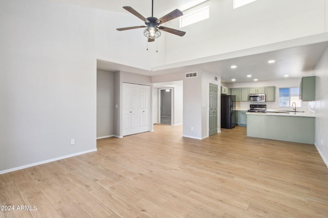 unfurnished living room featuring ceiling fan, sink, light hardwood / wood-style floors, and a high ceiling