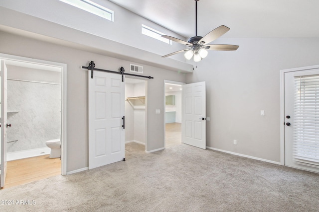 unfurnished bedroom featuring ceiling fan, a spacious closet, a barn door, ensuite bathroom, and light carpet