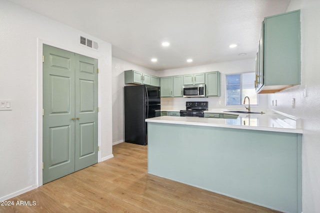 kitchen with black appliances, light hardwood / wood-style floors, kitchen peninsula, and sink