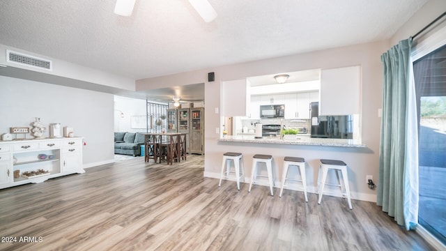 kitchen featuring black appliances, kitchen peninsula, tasteful backsplash, a kitchen bar, and white cabinetry