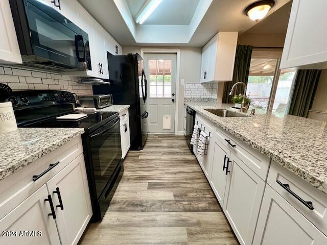 kitchen featuring black appliances, white cabinets, light stone countertops, and sink