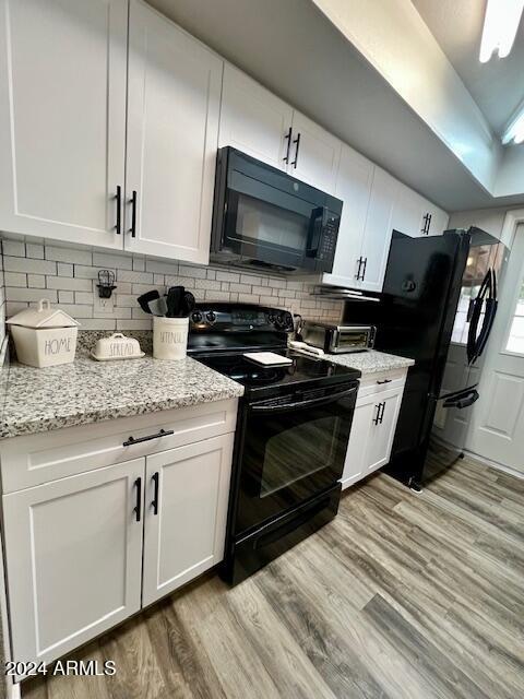 kitchen with black appliances, light hardwood / wood-style flooring, decorative backsplash, light stone counters, and white cabinetry