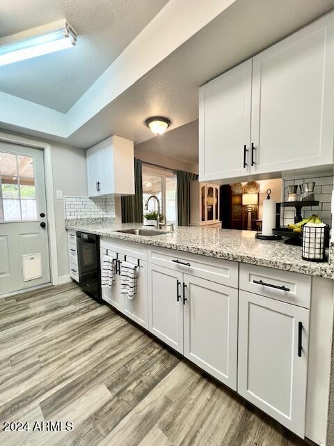 kitchen featuring sink, light stone countertops, black dishwasher, tasteful backsplash, and white cabinetry