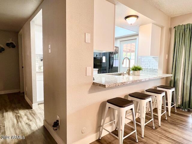 kitchen with white cabinets, a kitchen breakfast bar, black refrigerator, light hardwood / wood-style flooring, and light stone countertops