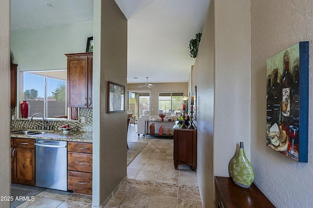 kitchen with light stone counters, a sink, open floor plan, stainless steel dishwasher, and decorative backsplash