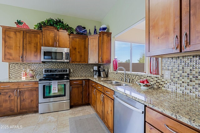 kitchen featuring brown cabinets, a sink, light stone countertops, stainless steel appliances, and backsplash