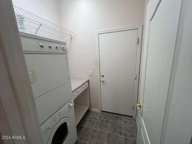 laundry room featuring stacked washer and clothes dryer and dark tile patterned floors