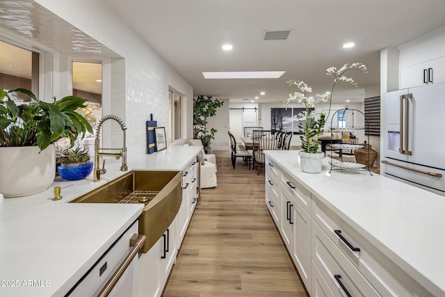 kitchen featuring white cabinetry, a skylight, light hardwood / wood-style floors, sink, and high end fridge