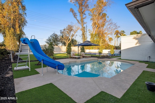 view of pool with a water slide, a lawn, and a patio