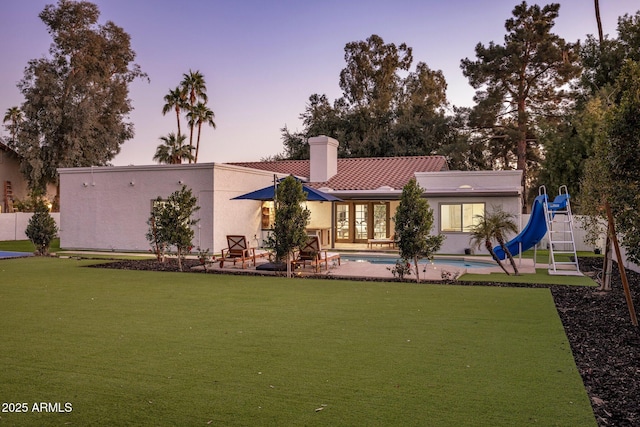 back house at dusk featuring a lawn